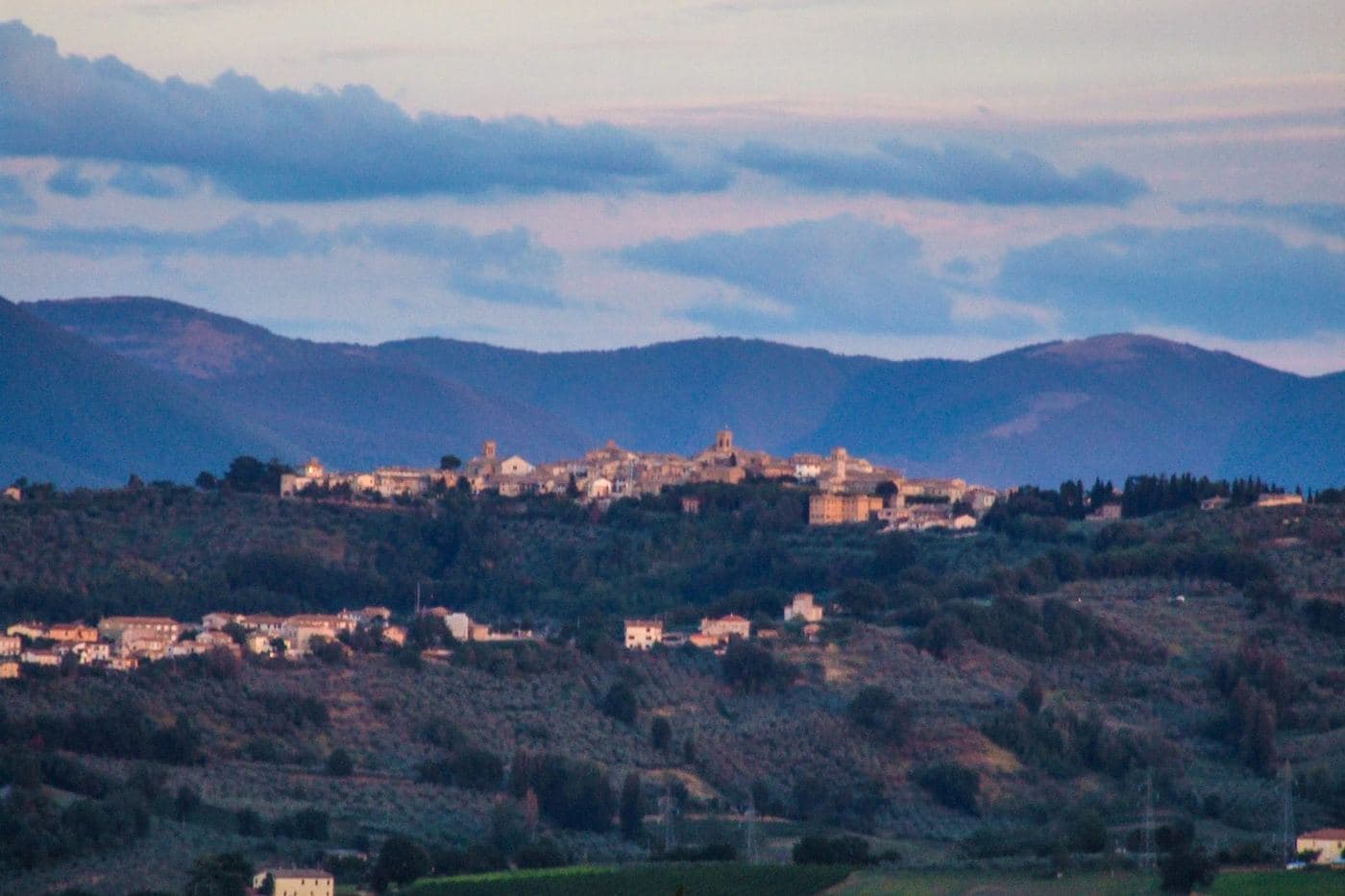 Montefalco no alto da colina ao entardecer, com campos e montanhas
