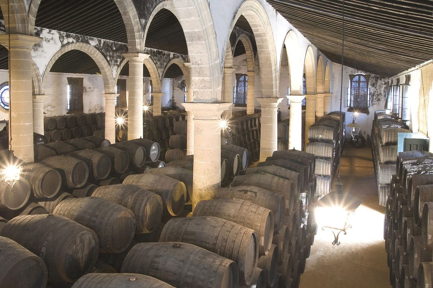 Fileiras de botas de Jerez empilhadas em níveis numa bodega com arcos