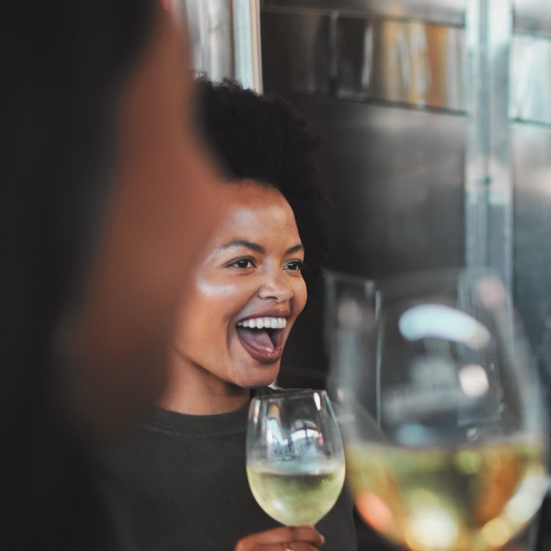 Mulher sorri com uma taça de vinho branco