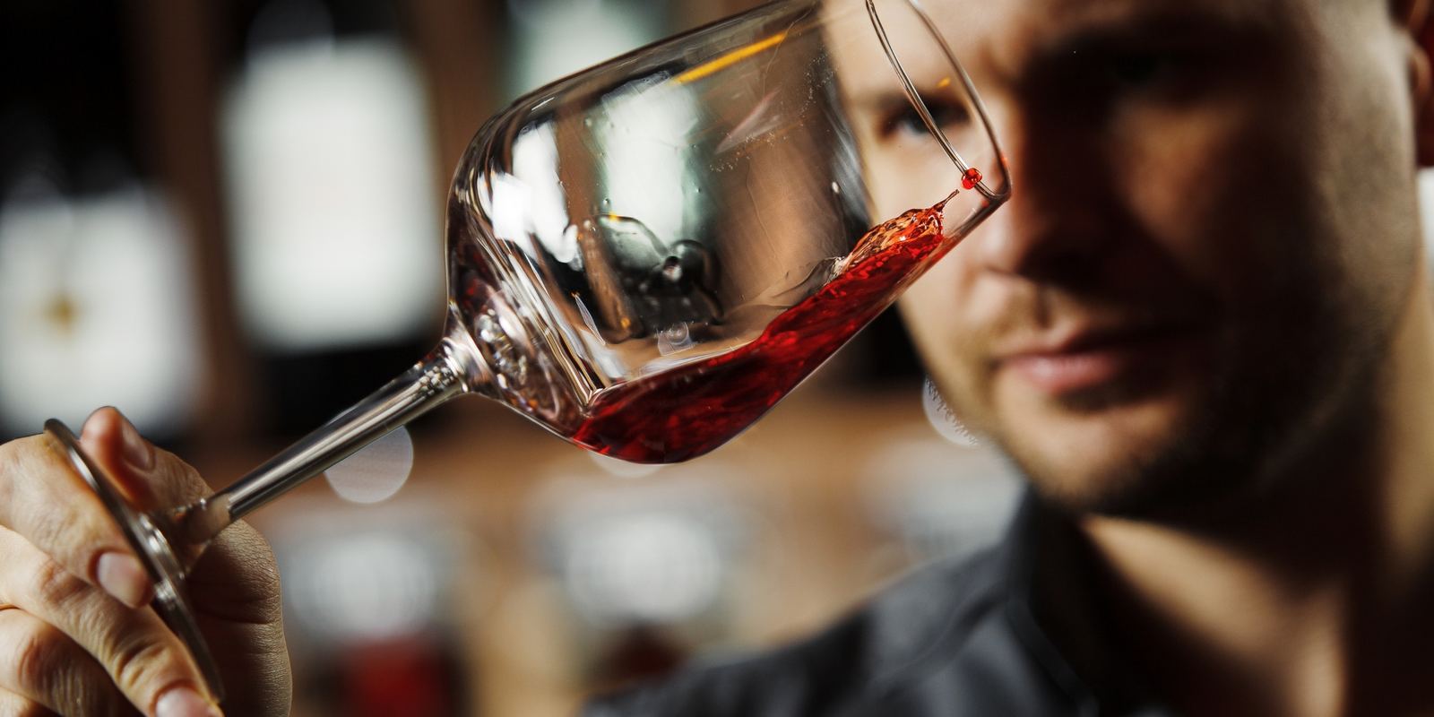 Taça de vinho tinto inclinada contra a luz, com o vinho girando, observada de perto
